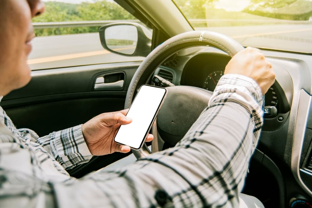 Driver texting on phone while operating a vehicle, illustrating the perils of distracted and irresponsible driving.