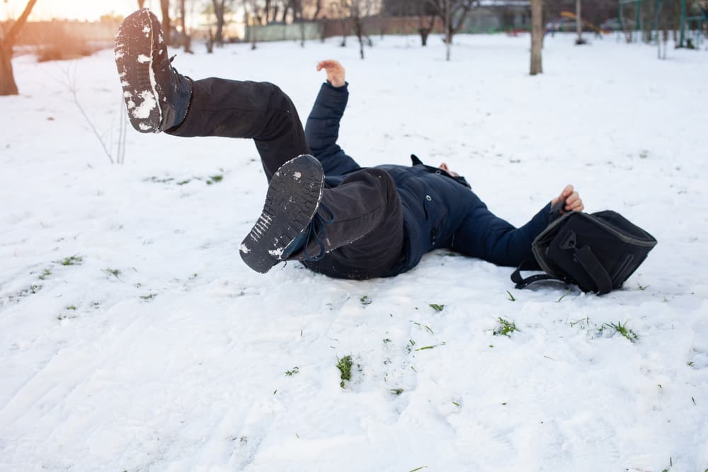 A man slips and falls in the snow, injured from the icy surface. Winter accident resulting in a possible fracture, bruise, or dislocation.
